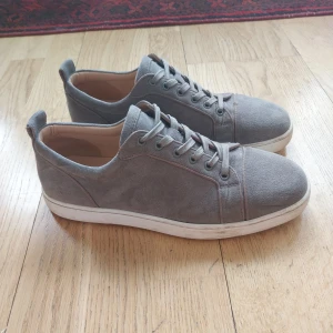 Gråa sneakers från Christian Louboutin - Snygga grå sneakers i mocka från Christian Louboutin med den ikoniska röda sulan. Skorna har snörning och en stilren design, storlek 43 men passar nog lite större också 