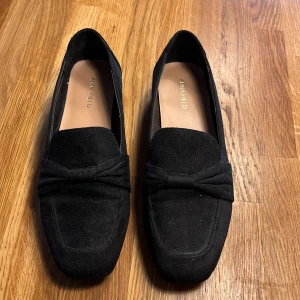 Svarta loafers från Anna Field - Snygga svarta loafers från Anna Field i mocka med en elegant rosett på ovansidan. Perfekta för en stilren look. Skorna har en klassisk design med låg klack och en bekväm passform.