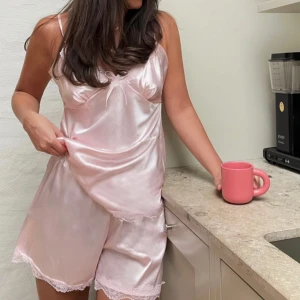 Missäy pyjamas siden. - Säljer ett elegant rosa linne i siden med spetsdetaljer och smala axelband. Linnet har en söt rosett framtill och är perfekt för en lyxig känsla. Matchande shorts ingår. Lite sönder vid tröjan men  annars bra skick. Storlek S