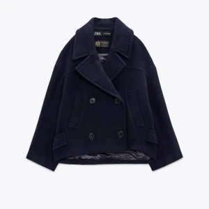 Ull kappa Zara - Snygg mörkblå kappa i ull från Zara med dubbelknäppning och bred krage. Jackan har en klassisk design med två framfickor och är perfekt för kyligare dagar. Tillverkad i samarbete med Manteco för en lyxig känsla. Nypris 1395kr