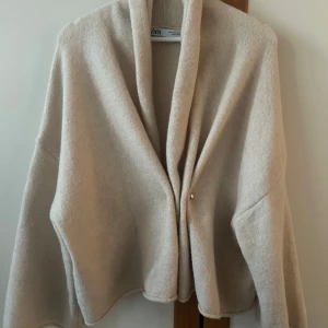 Beige cardigan från Zara - Säljer en stilren beige cardigan från Zara. Den har en enkel design med långa ärmar och en diskret knäppning framtill. Perfekt för att hålla sig varm och snygg under kyligare dagar.