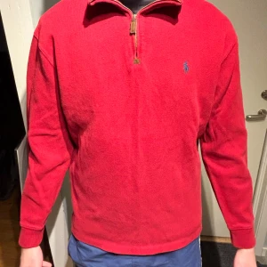 Röd tröja från Ralph Lauren - Säljer en snygg röd tröja från Ralph Lauren med dragkedja vid halsen och broderad logotyp på bröstet. Tröjan har långa ärmar och är perfekt för en stilren look.