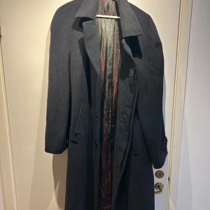 Mörkgrå kappa från Prandina - Elegant mörkgrå kappa från Prandina i en lyxig ull- och kashmirblandning. Kappan har en klassisk design med långa ärmar och knappar framtill. Köptes i en italiensk marknad år 2015 för 450€. Den är en overzied Stolek M