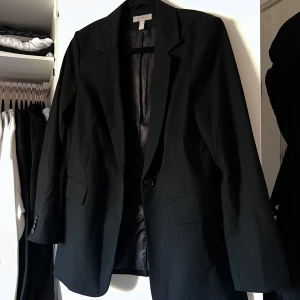 Svart kavaj - Snygg svart kavaj från H&M i klassisk design. Kavajen har en enkelknäppning med en knapp och tre knappar vid ärmsluten. Perfekt för en stilren look. Använd max 3 gånger. Önskar du veta exakta mått? Tveka inte att höra av dig!