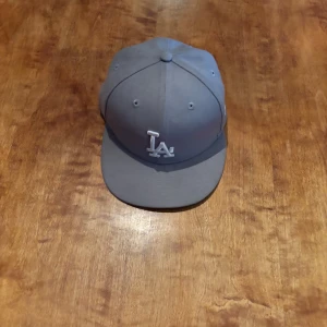 Grå keps från New Era - Snygg grå keps från New Era med broderad logotyp framtill. Kepsen är tillverkad i polyester och har en klassisk design med böjd skärm. Perfekt för en stilren look.