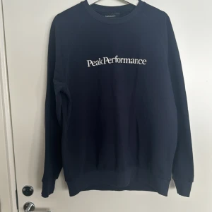 Mörkblå sweatshirt från Peak Performance - Säljer en stilren mörkblå sweatshirt från Peak Performance med deras logga tryckt på bröstet. Tröjan har långa ärmar och en klassisk rund halsringning. Perfekt för en avslappnad stil. Storlek L men passar en M. 