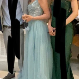 Ljusblå balklänning  -  ljusblå långklänning med glittrande paljetter på överdelen. Klänningen har en  v-ringad design  vilket ger en stilren och festlig look. Perfekt för bal eller andra speciella tillfällen. Köpt för 1150kr