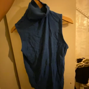 Blå ärmlös polotopp - Snygg blå ärmlös polotopp med hög krage. Perfekt för lager-på-lager eller som den är under varmare dagar. Enkel och stilren design som passar till många olika outfits.
