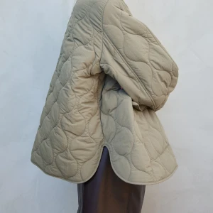 Grön quiltad jacka med dragkedja - Säljer en snygg beige quiltad jacka med dragkedja och stora fickor framtill. Jackan har en rundad krage och en avslappnad passform som ger en cool look! 