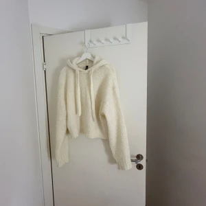 Vit stickad hoodie från H&M - Mysig vit stickad hoodie från H&M. Den har en luva och långa ärmar, perfekt för kyliga dagar. Tröjan är croppad och har en avslappnad passform. Perfekt för en casual look!