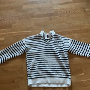 Randig tröja från Tommy Hilfiger, använt 2-3 gånger. Storlek- 176! - Säljer en snygg randig tröja från Tommy Hilfiger i vitt och marinblått. Tröjan har en halfzip! Det är ett fint, snygg material på tröjan!