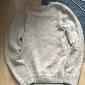 Beige tröja från Bondelid - Säljer en stilren beigetröja från Bondelid. Tröjan har långa ärmar och en diskret broderad logga på bröstet. Perfekt för kyligare dagar med sin mjuka och bekväma passform. Passar utmärkt till både jeans och chinos.