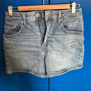 Blå jeansshorts - Säljer ett par klassiska blå jeansshorts med hög midja. De har en knapp och dragkedja framtill samt fem fickor. Inte min stil riktigt men dem är fortfarande fina. Lite för stora för mig i midjan. Bra skick✨