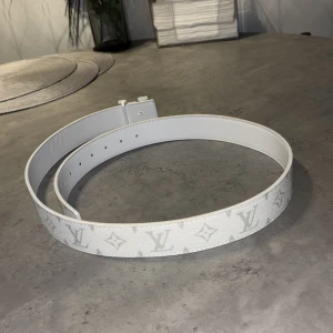 Vit monogram bälte från Louis Vuitton - Snyggt vitt bälte från Louis Vuitton med det klassiska monogrammönstret. Bältet har en stilren design med en vit LV-spänne framtill. Perfekt för att ge en lyxig touch till din outfit.