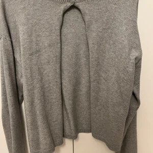 Grå stickad kofta från bikbok - Säljer en stilren grå stickad kofta från bikbok. Koftan har en unik design med en öppning framtill och långa ärmar. 