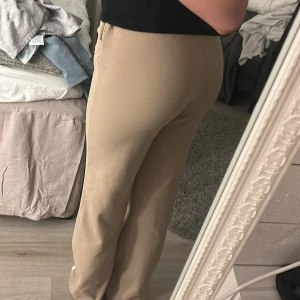 Beigea kostymbyxor från Vero Moda - Snygga beige byxor från Vero Moda i storlek S. Byxorna har en rak passform och är tillverkade i ett mjukt material som ger en bekväm känsla. Perfekta för en stilren look.