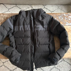 Svart pufferjacka från Helly Hansen - Säljer en svart skidjacka från Helly Hansen. Helt oanvänd, inköpt förra säsongen. Oroligt bekväm, varm jacka i strl: L som passar perfekt till både skidresan och när som helst. Nypris: 3000kr, pris nu 749. Hör bara av dig vid frågor eller fler bilder