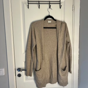 Beige kofta från VILA - Säljer en stilren beige kofta från VILA i storlek XS. Koftan har långa ärmar och två praktiska fickor framtill. Perfekt för lager-på-lager under kyligare dagar. Den är mjuk och bekväm, vilket gör den till ett mångsidigt plagg i garderoben.