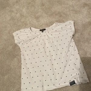 Vit prickig topp från Marine - Säljer en söt vit topp från Marine med svarta prickar. Toppen har korta ärmar och en rund halsringning. Perfekt för en avslappnad stil. 🖤