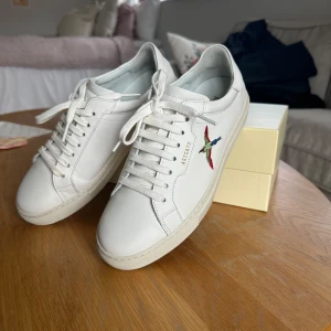 Vita sneakers från Axel Arigato - Snygga vita sneakers från Axel Arigato med broderad fågel på sidan.  Modell 180 clean . Väldigt fint skick, endast använda 3 ggr. Säljer då de inte passar.🩷 original förpackning finns! Nypris 2600! 