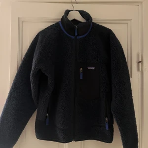 Mörkblå fleecejacka från Patagonia - Säljer en mörkblå fleecejacka från Patagonia med blå detaljer.  Nypris 2595kr  En ficka sönder men i övrigt väldigt fint skick.   Djur och rökfritt hem.