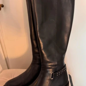 Svarta höga stövlar i skinn - Snygga svarta höga stövlar i skinn med dekorativa nitar runt ankeln. Perfekta för en stilren look och passar bra till både jeans och kjol. används typ två gånger