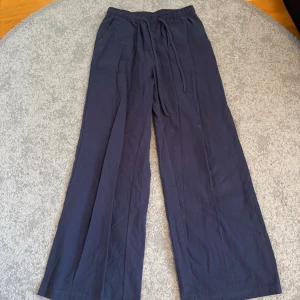 Mörkblå vida byxor med dragsko - Snygga mörkblå linne byxor med en avslappnad passform och dragsko i midjan. Perfekta för en bekväm och stilren look. Byxorna har en loose fit och är tillverkade i ett mjukt material.