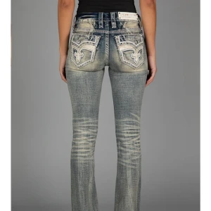 Blå jeans med broderade detaljer Rock Revival - Snygga blå jeans med unika broderade detaljer på bakfickorna. De har en klassisk femficksdesign och en lätt tvättad look. Perfekta för en avslappnad stil med en touch av personlighet. W24