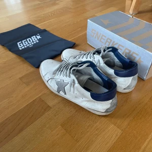 Golden goose blå vit - Snygga vita sneakers från GGDB med blåa detaljer. Skorna har snörning och en klassisk design som passar perfekt för en avslappnad stil. De kommer med originalförpackning och påse. Slitna vid undersidan, se bild 