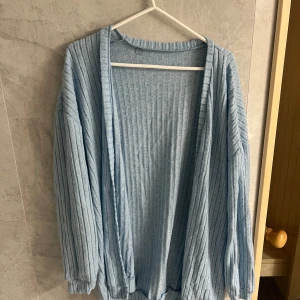 Ljusblå ribbad kofta - Säljer en ljusblå ribbad kofta med långa ärmar. Perfekt för en avslappnad stil och passar bra till både jeans och kjol. Koftan är öppen framtill och har en mjuk och bekväm känsla.
