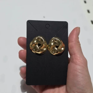 Guldiga örhängen i flätad design - Snygga guldiga örhängen med en unik flätad design. Perfekta för att ge en elegant touch till din outfit. De är runda och har en glansig yta som fångar ljuset fint.