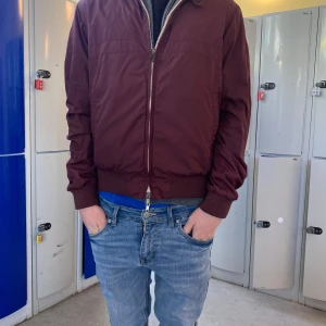 Moncler windbrekar - Säljer en snygg vinröd windbrekar från Moncler. Jackan har en dragkedja framtill och ett broderat Moncler-märke på ärmen. Den är långärmad med ribbade muddar och nederkant. Perfekt för höst och vår! Hör av er vid minsta fundering!✨