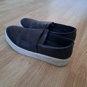 Svarta loafers från Vox - Snygga svarta loafers från Vox med en vit sula. Skorna har en stilren design och är perfekta för en avslappnad look. De är tillverkade i syntetmaterial och har en bekväm passform.