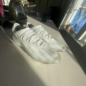 Vita fotbollsskor från Adidas - Säljer ett par vita fotbollsskor från Adidas med snörning och en stilren design. Skorna har en lätt och smidig konstruktion med dobbar för optimalt grepp på planen. Perfekta för den som vill ha både stil och funktionalitet på fotbollsplanen.