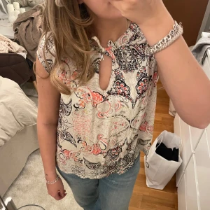 Odd Molly Blus - Säljer en färgglad blus från odd molly med ett unikt mönster i svart, rosa och orange. Blusen har korta ärmar och en knytning vid halsen som ger en fin detalj. storlek vilket motsvarar S! pris går att diskutera och är öppen för byten!🤍