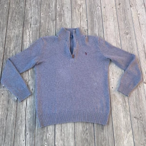Grå 1/4 zip från Polo Ralph Lauren - Säljer en stilren grå tröja från Polo Ralph Lauren. Tröjan har en dragkedja vid halsen och är tillverkad i ett mjukt material. Perfekt för kyligare dagar med sin långärmade design och ribbade detaljer vid ärmslut och nederkant. storlek XS men passar även S. Mycket bra skick!