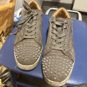 Grå loubs - Snygga grå sneakers med nitar på ovansidan och en ikonisk röd sula. Skorna har snörning och en cool design som sticker ut. Perfekta för dig som vill ha en edgy stil. Ett par spikar saknas därav priset. PRIS GÅR OCH DISKUTERA