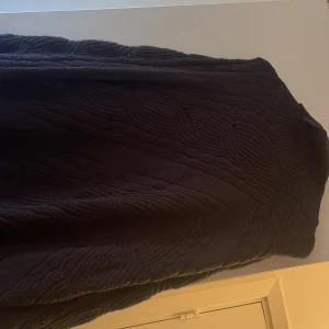 Svart stickad tröja - Säljer en svart stickad tröja med ett snyggt kabelstickat mönster. Perfekt för kyliga dagar och ger en stilren look. Tröjan har en hög krage och långa ärmar som håller dig varm och bekväm. Man har den över en annan tröja 