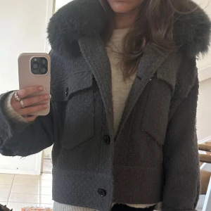Meotine jacka - Snygg grå meotine charlie jacka med en lyxig pälsdetalj på kragen. Jackan har ett diskret mönster och knäpps med stora svarta knappar. Två fickor framtill ger en cool look. Den är i stl XS/S. den är lite nopprig. Pälsen går att ta av