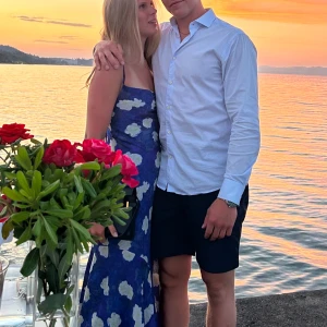 Blå blommig klänning från ADOORE - Säljer en vacker blå klänning från ADOORE med vita blommor. Klänningen har smala axelband och knytning i ryggen/ öppen rygg. Perfekt för sommarens festligheter! 🌸