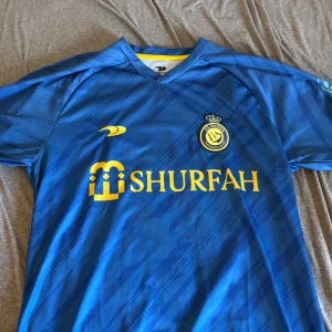 Al Nassr Fotbollströja Ronaldo - En fet Ronaldo tröja från Al Nassr! OBS! Tröjan är köpt från Turkiets marknad det vill säga att den inte är äkta! Tröjan är passar till storlek M men på tröjan står det XL. Har själv storlek L fast den sitter ändå lite för tight så det är en M!