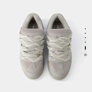 Snygga grå sneakers med breda snören och en stilren design. Skorna har en robust sula och är perfekta för en avslappnad stil. De är tillverkade i syntetmaterial och har en modern look. Skorna är från Bershka! Knappast använda. Skorna är för män.