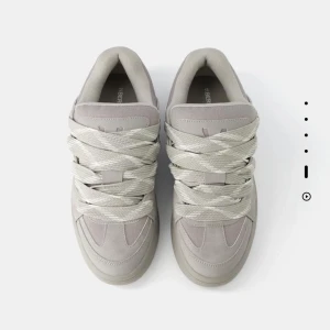 Gråa skor från Bershka  - Snygga grå sneakers med breda snören och en stilren design. Skorna har en robust sula och är perfekta för en avslappnad stil. De är tillverkade i syntetmaterial och har en modern look. Skorna är från Bershka! Knappast använda. Skorna är för män.