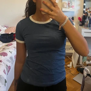 Blå t-shirt med vita detaljer  - Säljer en snygg blå t-shirt med vita kanter vid hals och ärmar. Perfekt för en avslappnad stil. Passar till det mesta och är superbekväm!