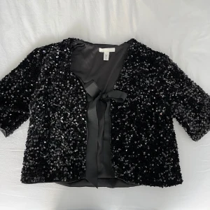 Svart paljettkofta från H&M - Snygg svart paljettkofta från H&M med trekvartsärm och knytband framtill. Aldrig använd 