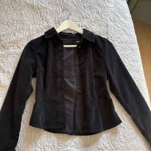 Svart manchesterjacka från ASOS DESIGN - Snygg svart manchesterjacka från ASOS DESIGN med knappar framtill. Jackan har en klassisk krage och långa ärmar, perfekt för en stilren look.