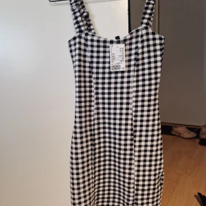 Svartvit rutig klänning - Snygg svartvit rutig klänning med axelband. Perfekt för en stilren look. Klänningen har en klassisk design som passar till många tillfällen.