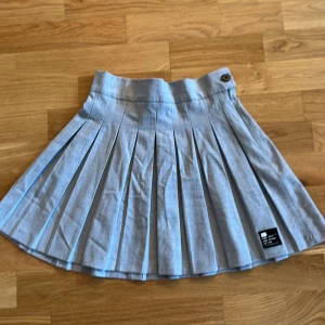 Grå plisserad kjol från Bershka - Snygg grå plisserad kjol från Bershka med en knappdetalj i midjan. Perfekt för sommaren och nästan aldrig använ