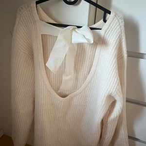 Stickad tröja med öppen rygg och rosett - Jättefin populär vit stickad tröja med öppen rygg och rosett. Perfekt till våren. Endast använd 2 gånger. Superbra kvalitet. Slutsåld på hemsidan, köpte för 499kr.☺️