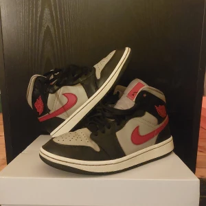 Nike Air Jordan 1 Mid i svart och röd - Snygga Nike Air Jordan 1 Mid sneakers i svart och röd med grå detaljer. Perfekta för dig som vill ha en stilren och sportig look. Skorna har den klassiska Air Jordan-loggan och en bekväm passform.
